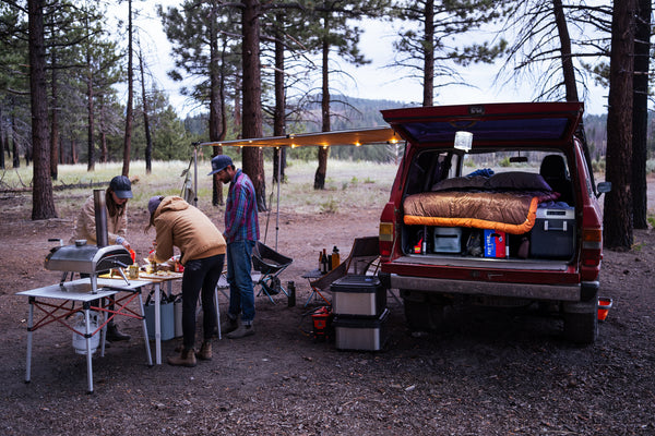 cool camping setup with friends cooking pizza on an ooni oven outside